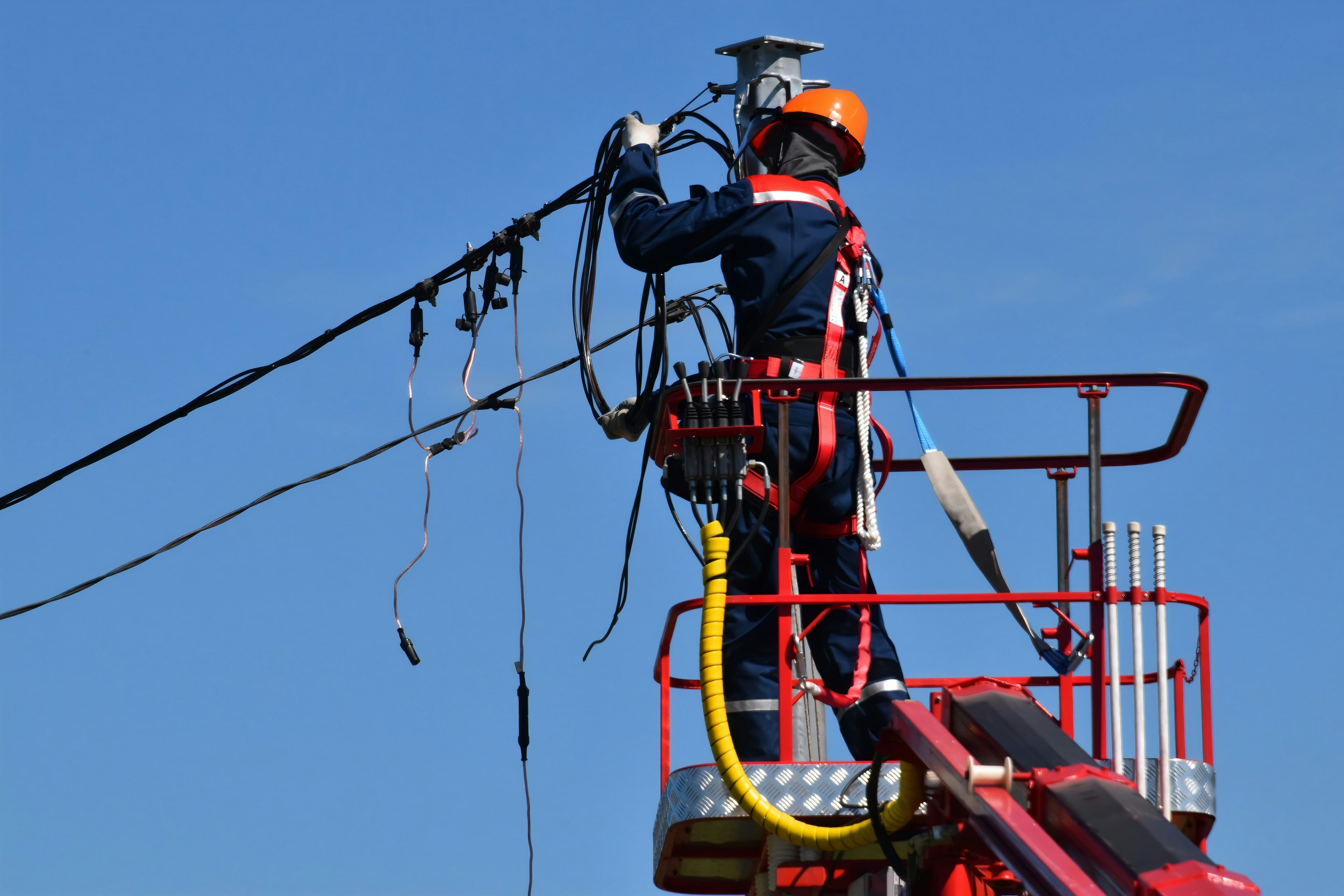 Representative photograph of a worker servicing overhead electrical cables from an elevated platform.